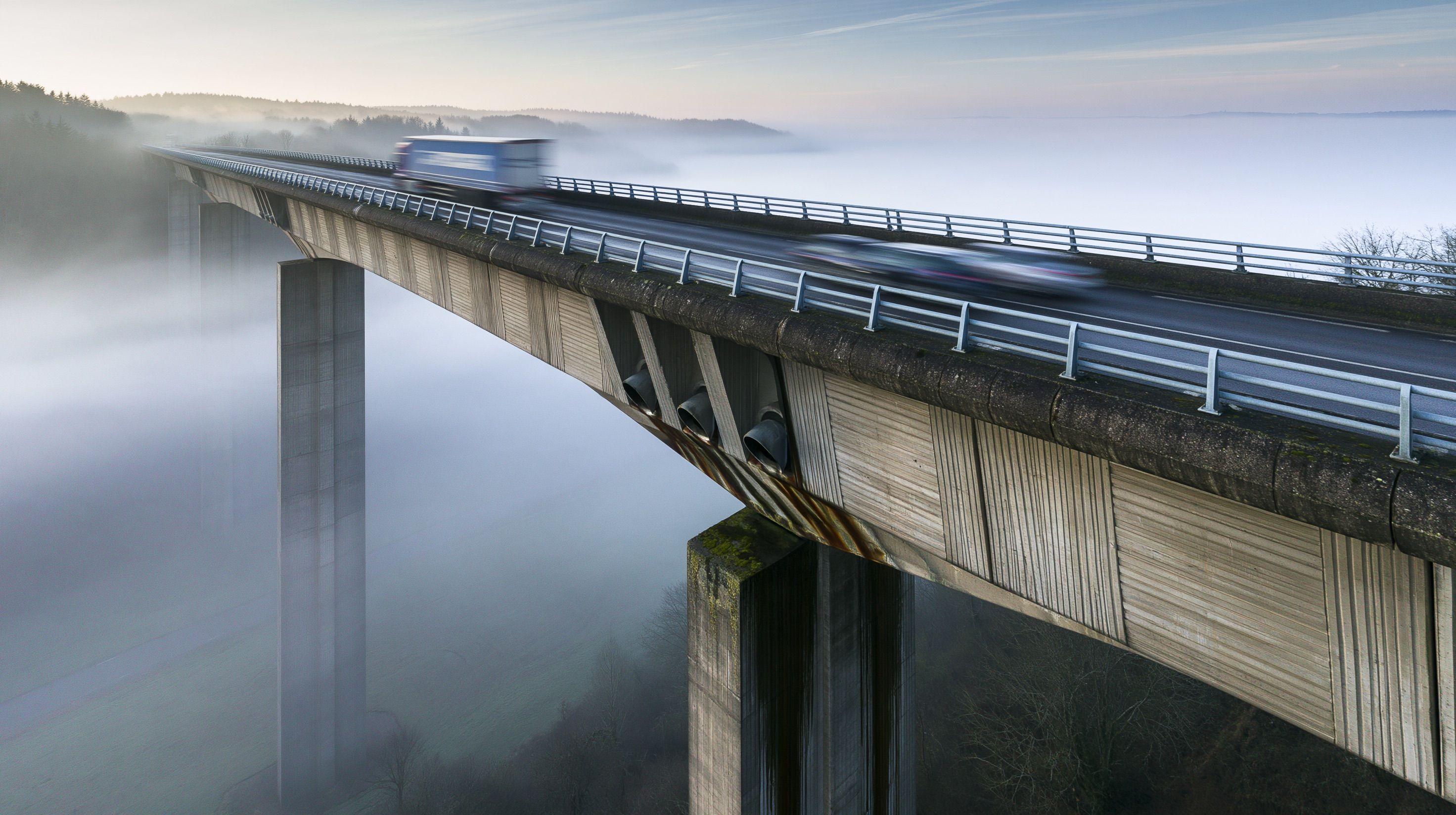 Viaduc de pierre vu du ciel à hauteur de tablier, ses arches alignées dans la lumière rasante d'un matin d'hiver, la vallée en dessous noyée de brume.