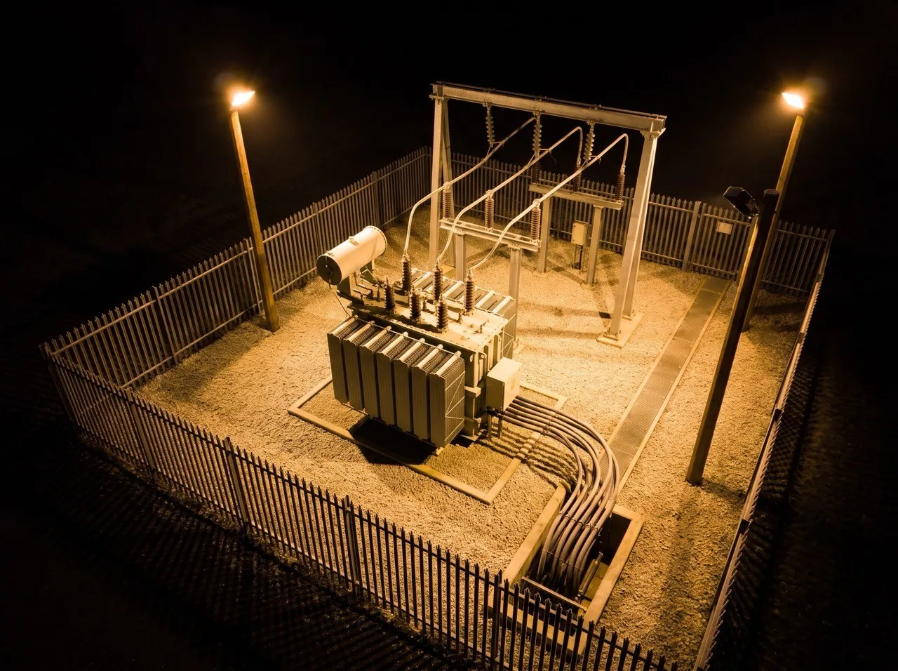 Poste électrique et son transformateur, éclairés de nuit.