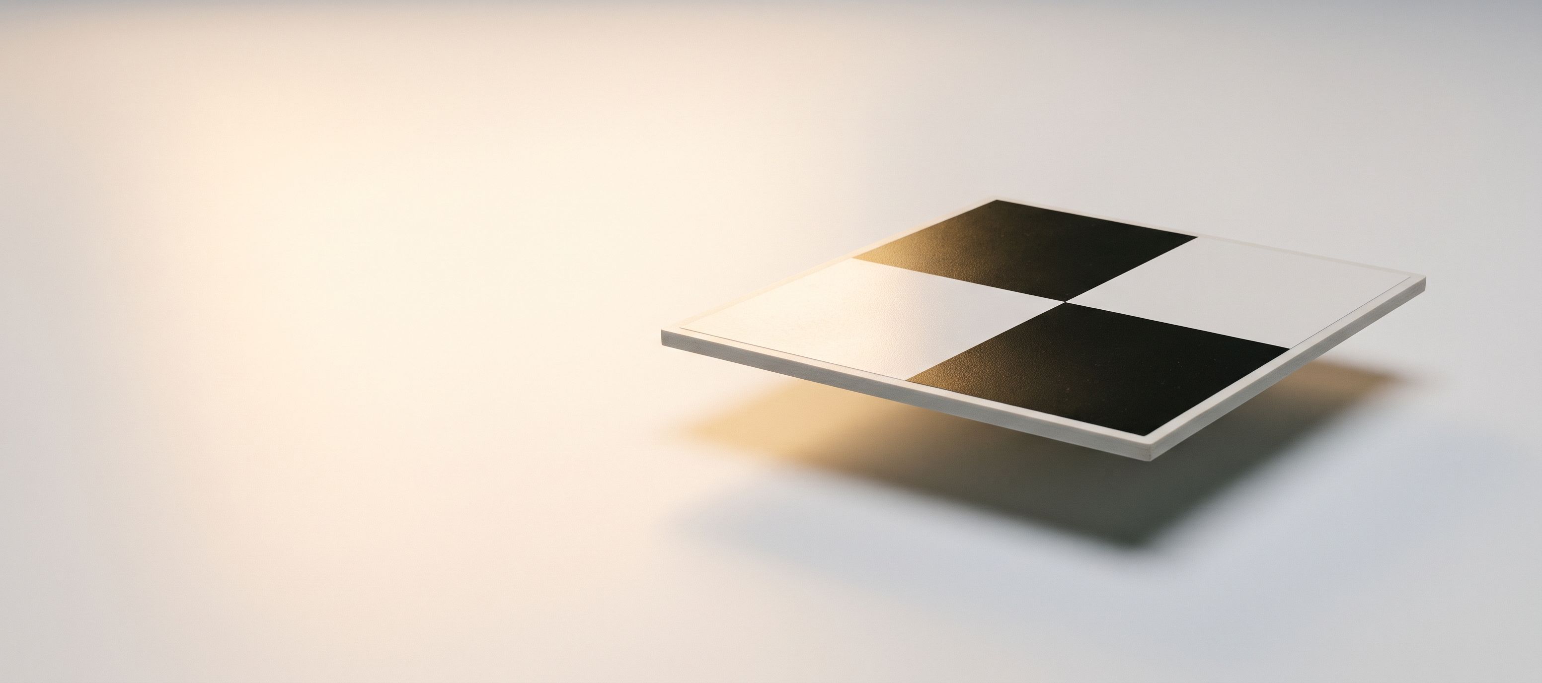 Une cible d'appui en damier noir et blanc, en suspension au-dessus d'un fond blanc, dans une lumière dorée rasante.
